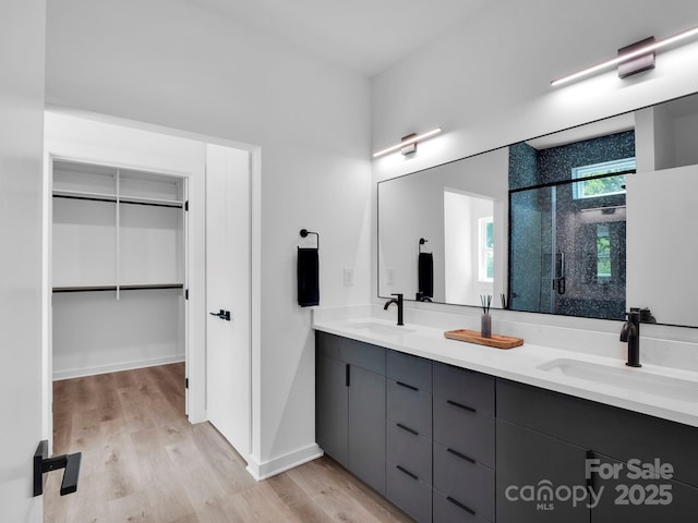 bathroom with double vanity, a shower stall, a sink, and wood finished floors