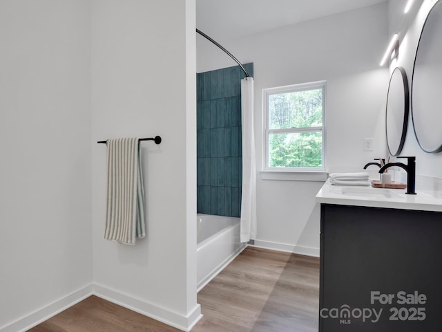 bathroom featuring double vanity, shower / bath combo, wood finished floors, a sink, and baseboards