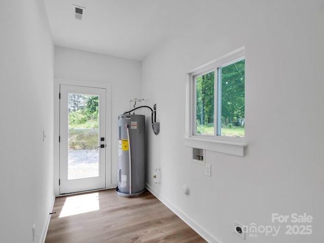 doorway to outside featuring baseboards, water heater, wood finished floors, and visible vents