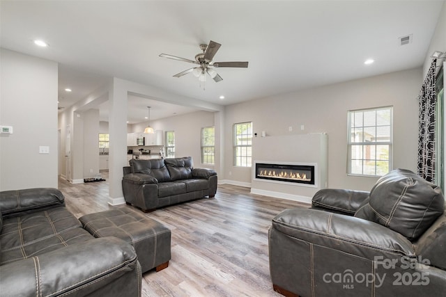living area featuring light wood-type flooring, a ceiling fan, visible vents, and a wealth of natural light