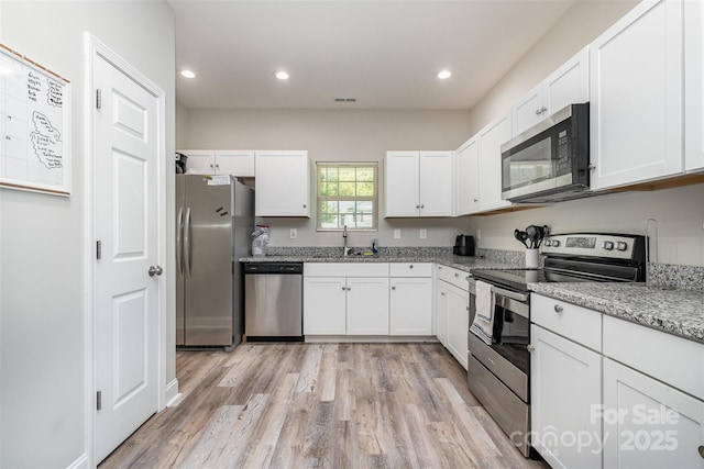 kitchen with light wood-type flooring, appliances with stainless steel finishes, a sink, and white cabinets