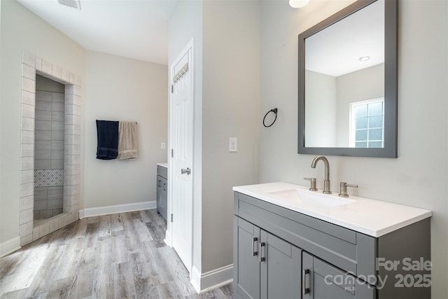 bathroom with visible vents, baseboards, vanity, wood finished floors, and tiled shower