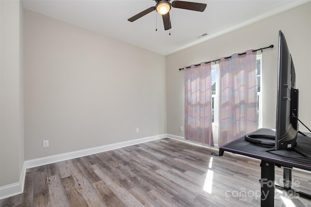 empty room with wood finished floors, ceiling fan, baseboards, and visible vents