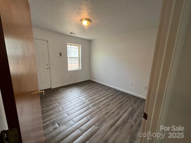 empty room featuring visible vents, a textured ceiling, baseboards, and dark wood-style floors