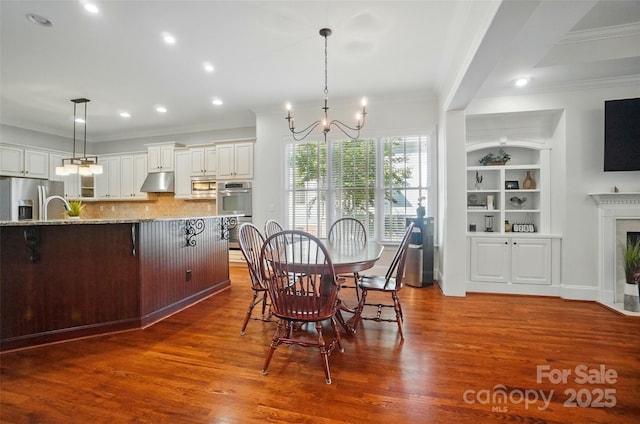 dining room with a notable chandelier, a fireplace, ornamental molding, recessed lighting, and dark wood-style floors