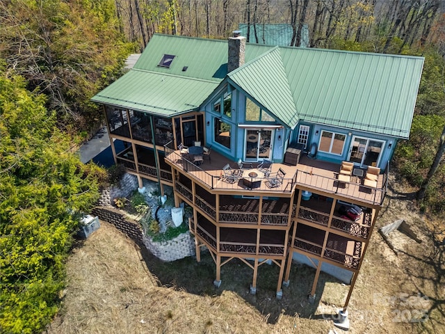back of house featuring a deck, a chimney, a forest view, a standing seam roof, and metal roof