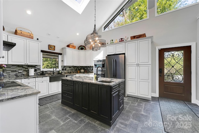 kitchen with white cabinets, a sink, high vaulted ceiling, freestanding refrigerator, and backsplash