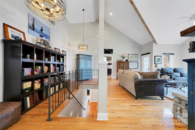 living area with wood finished floors, beamed ceiling, baseboards, high vaulted ceiling, and ceiling fan with notable chandelier