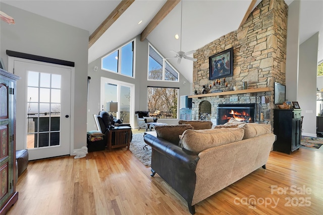 living room with beam ceiling, high vaulted ceiling, a stone fireplace, light wood-style flooring, and a ceiling fan