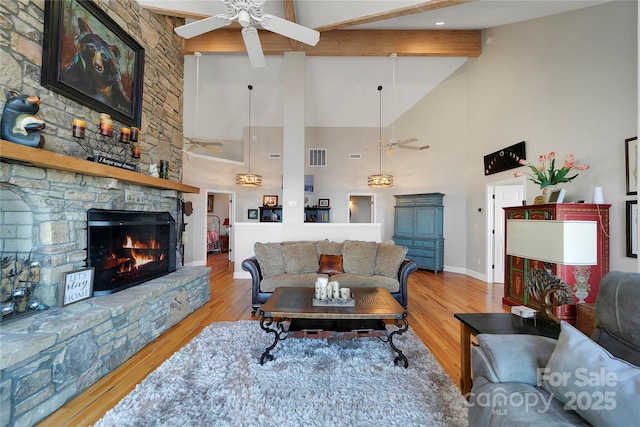 living room with a stone fireplace, ceiling fan, high vaulted ceiling, and beamed ceiling