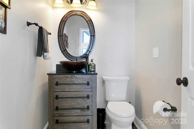 bathroom with an inviting chandelier, baseboards, vanity, and toilet