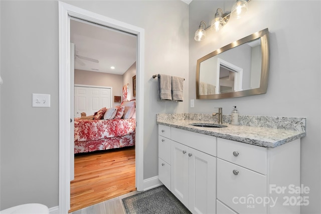 ensuite bathroom featuring ceiling fan, wood finished floors, vanity, baseboards, and ensuite bath