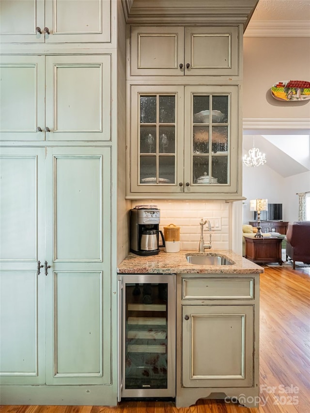 bar featuring a sink, a chandelier, light wood-style floors, crown molding, and beverage cooler