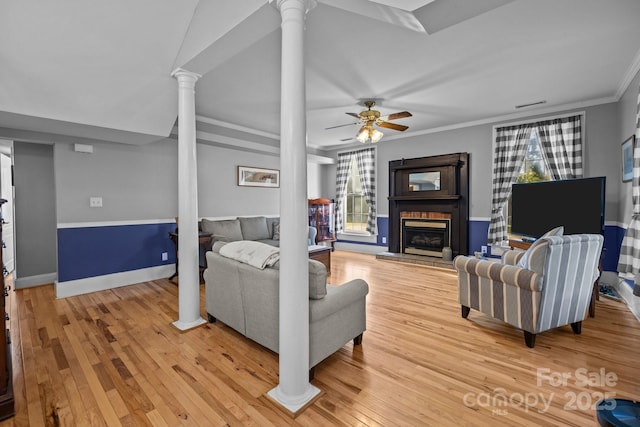 living area featuring ceiling fan, a fireplace, decorative columns, light wood-type flooring, and ornamental molding