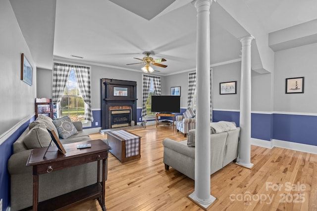 living room with decorative columns, a fireplace with raised hearth, a healthy amount of sunlight, and ceiling fan