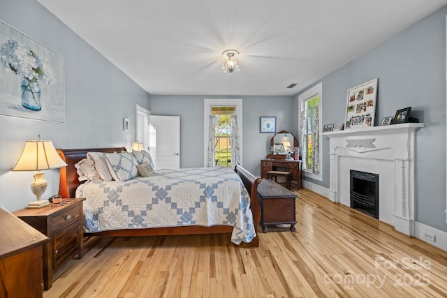 bedroom featuring a fireplace, visible vents, hardwood / wood-style flooring, and baseboards
