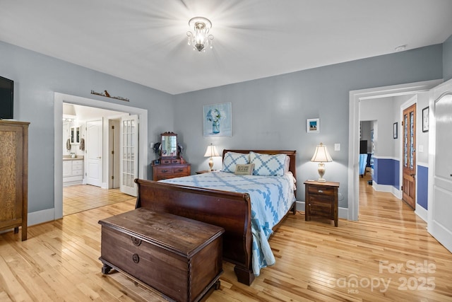bedroom with light wood-style flooring, ensuite bathroom, and baseboards