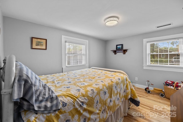 bedroom with wood finished floors, baseboards, multiple windows, and visible vents