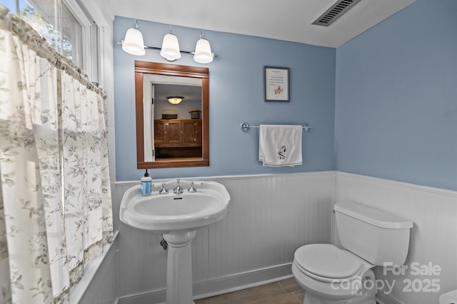 bathroom featuring shower / bath combo with shower curtain, a wainscoted wall, visible vents, and toilet