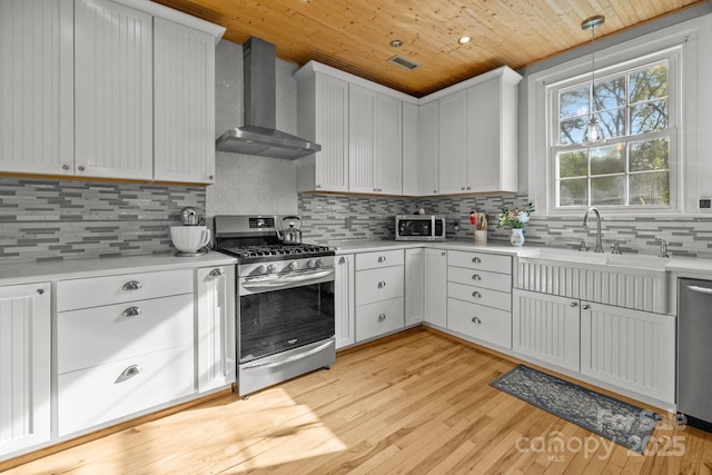 kitchen with light countertops, wood ceiling, appliances with stainless steel finishes, and wall chimney range hood