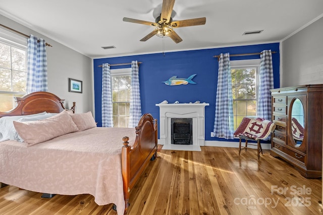 bedroom with a fireplace with flush hearth, visible vents, hardwood / wood-style flooring, and ornamental molding