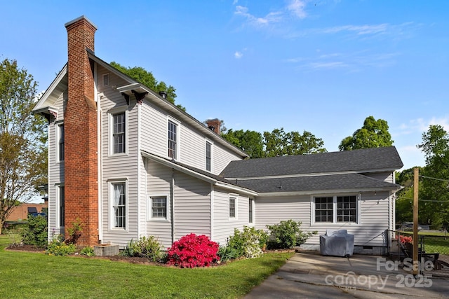 back of property featuring roof with shingles, a chimney, crawl space, a patio area, and a lawn