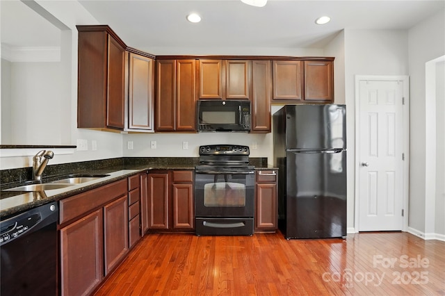 kitchen with a sink, dark stone countertops, recessed lighting, wood finished floors, and black appliances