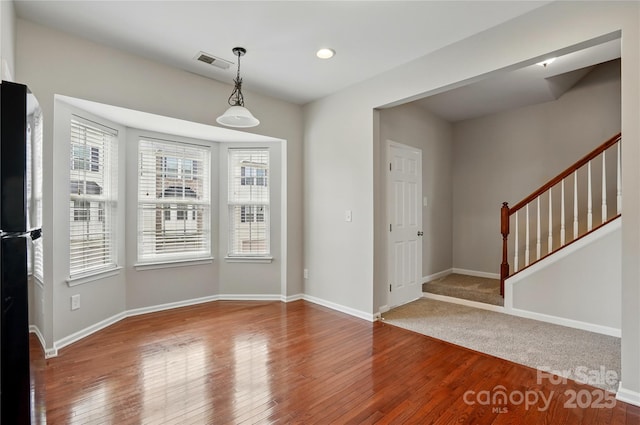 unfurnished dining area featuring baseboards, wood finished floors, visible vents, and stairway