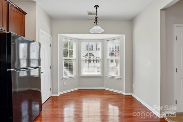 unfurnished dining area with wood-type flooring, visible vents, and baseboards