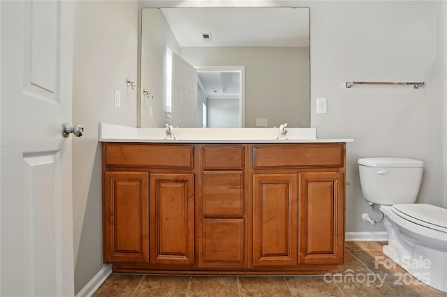 bathroom with toilet, a sink, double vanity, and baseboards