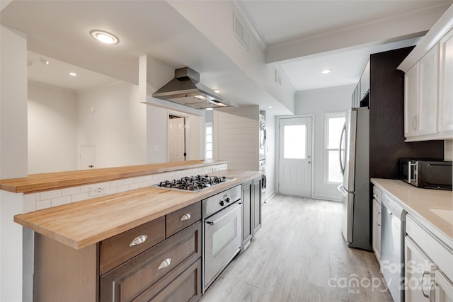 kitchen with white cabinets, wooden counters, stainless steel appliances, decorative backsplash, and island exhaust hood