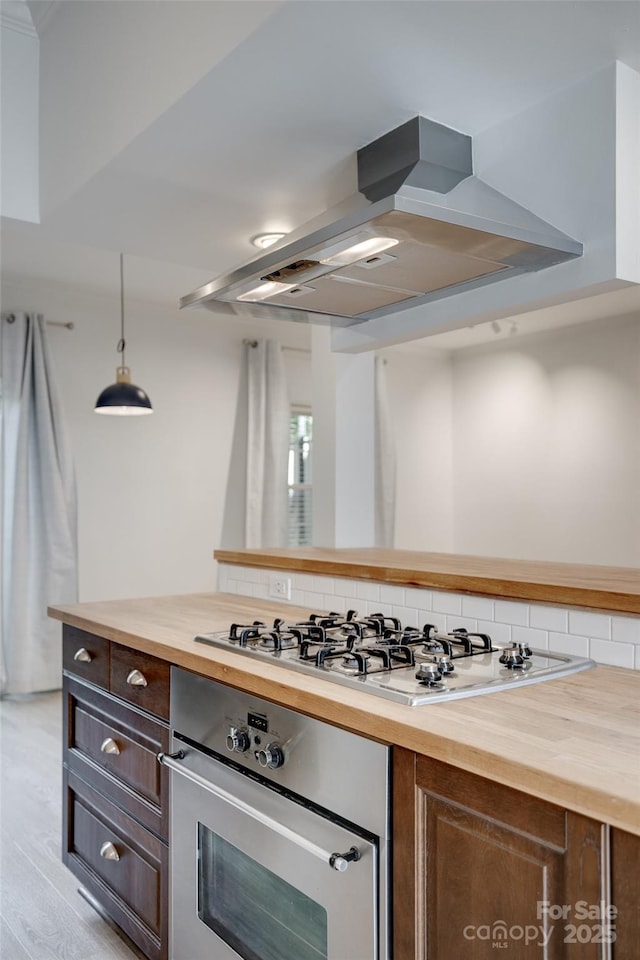kitchen with island exhaust hood, decorative backsplash, wood counters, and stainless steel appliances