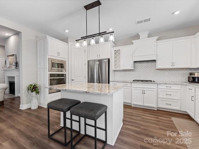 kitchen with decorative backsplash, a kitchen island, visible vents, white cabinets, and stainless steel appliances