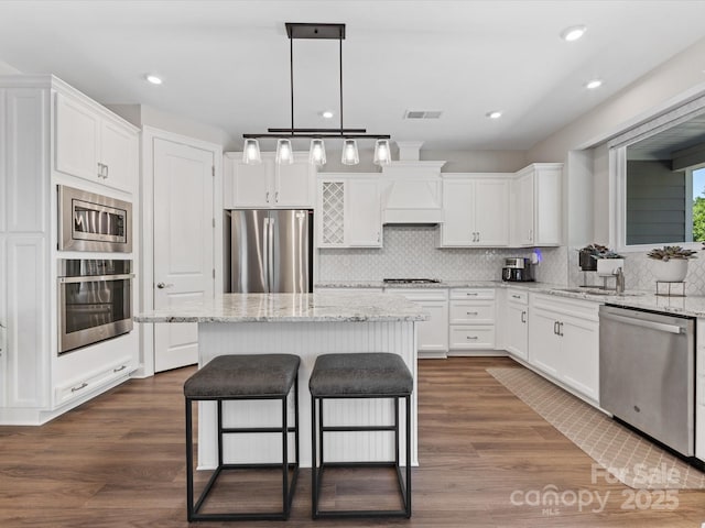 kitchen with a kitchen breakfast bar, stainless steel appliances, white cabinetry, a kitchen island, and visible vents