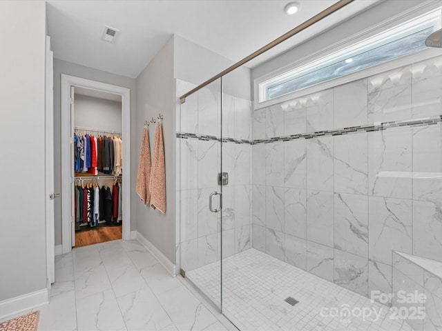 full bath featuring baseboards, a walk in closet, a stall shower, and marble finish floor