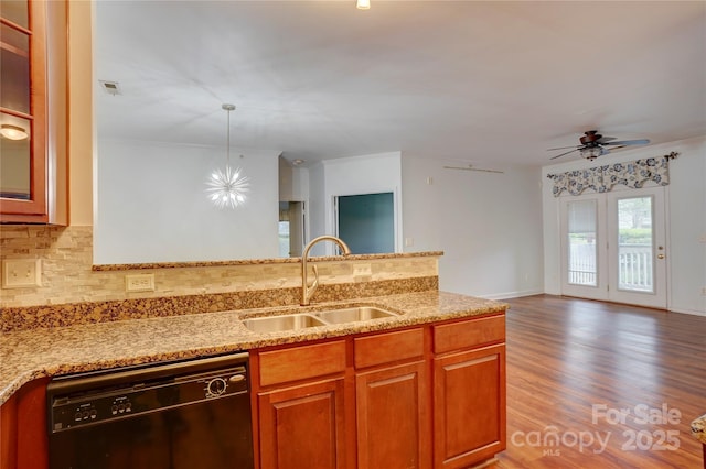 kitchen featuring decorative backsplash, light stone countertops, black dishwasher, and a sink