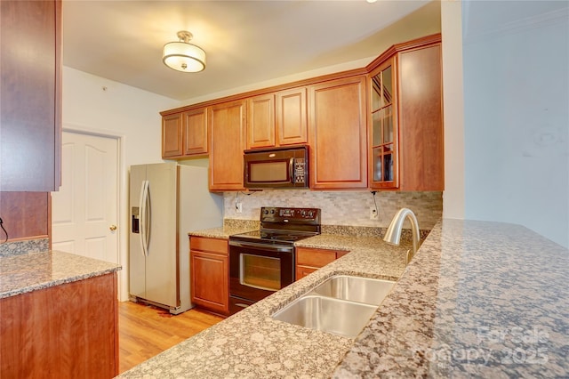 kitchen featuring a sink, backsplash, light wood-style floors, light stone counters, and black appliances