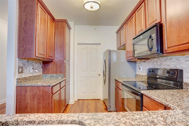 kitchen featuring light stone countertops, decorative backsplash, light wood-style flooring, and black appliances