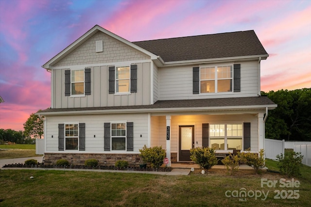 view of front facade featuring board and batten siding, stone siding, a front yard, fence, and a porch
