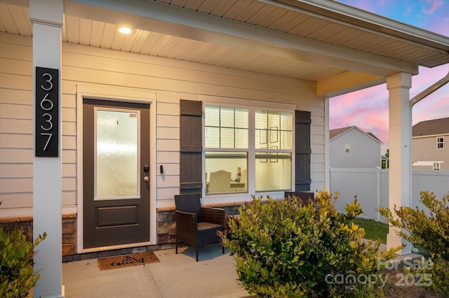 exterior entry at dusk featuring fence and stone siding