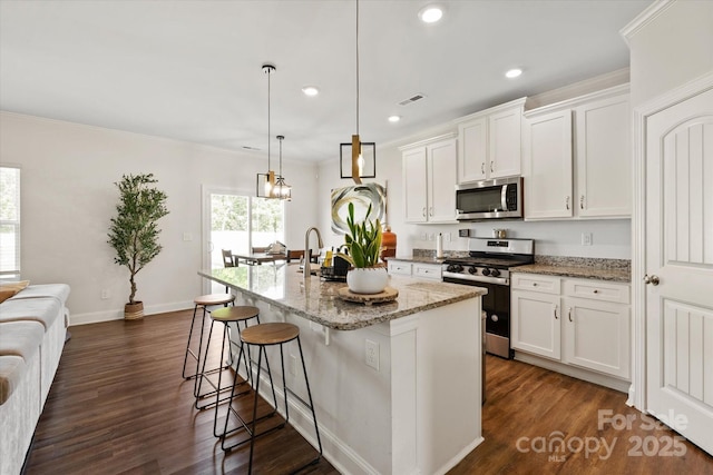 kitchen featuring a kitchen island with sink, light stone countertops, a kitchen bar, white cabinets, and appliances with stainless steel finishes