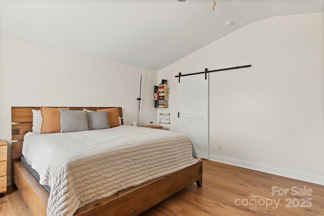 bedroom with a barn door, light wood-type flooring, vaulted ceiling, and baseboards