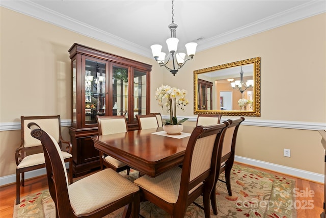 dining space with baseboards, a notable chandelier, crown molding, and light wood finished floors