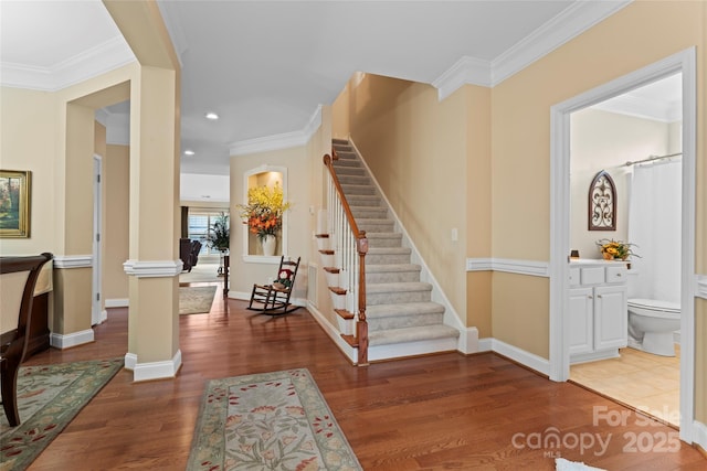 stairway featuring wood finished floors, crown molding, baseboards, and decorative columns