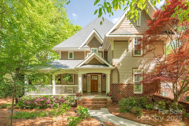 craftsman-style home featuring a shingled roof, covered porch, and brick siding
