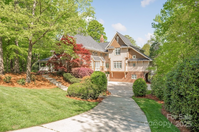 view of front of home with brick siding, driveway, a chimney, and a front yard