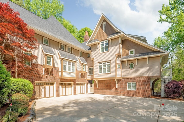 back of property with brick siding, driveway, roof with shingles, and a garage