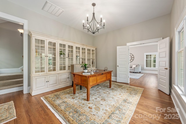 office with wood finished floors, visible vents, baseboards, and a notable chandelier
