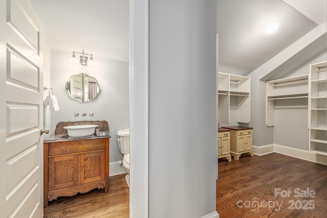 bathroom with toilet, vanity, wood finished floors, and baseboards
