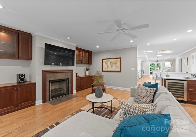 living area with beverage cooler, light wood finished floors, recessed lighting, ceiling fan, and a tile fireplace